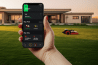 robot tondeuse Kress devant villa et en premier plan : main tenant un smartphone avec l'appli de pilotage